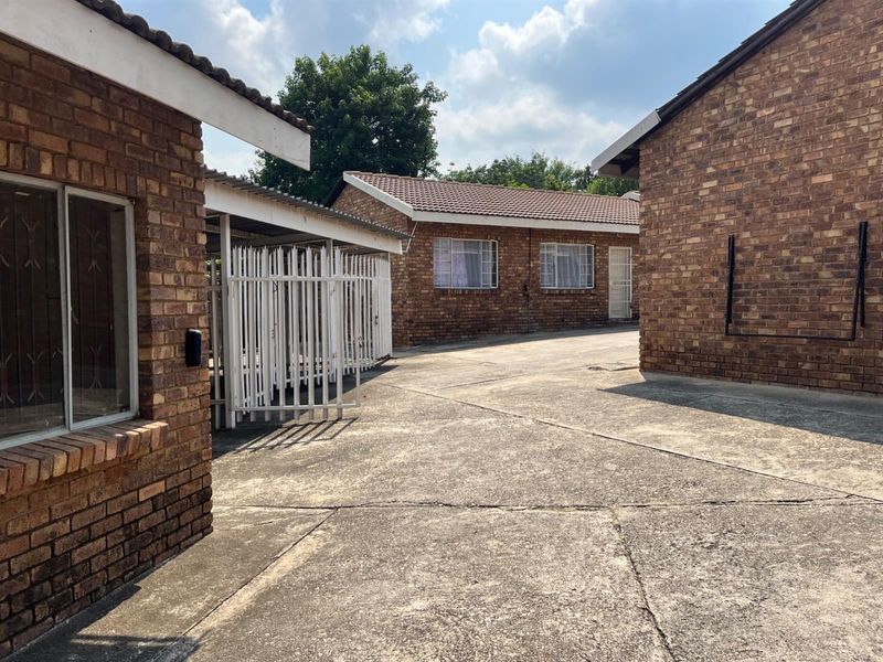 Exterior view of a face brick apartment complex featuring a concrete driveway, security gates, and tiled roofing.