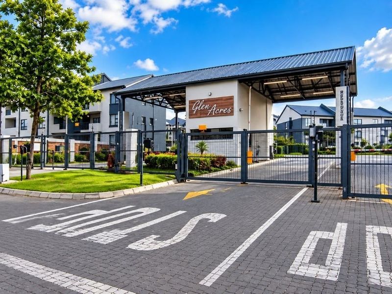 The main entrance and security gatehouse of the Glen Acres apartment complex, featuring paved access and modern perimeter fencing.