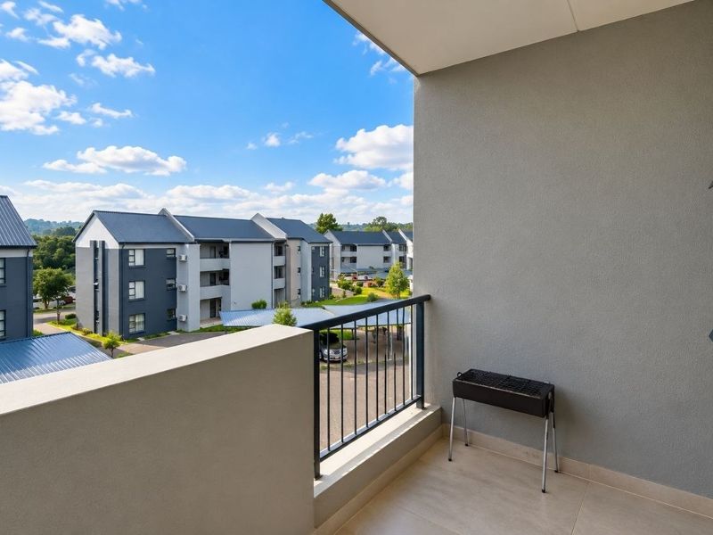 A clean, covered balcony featuring tiled flooring and a metal balustrade, offering an open view of the surrounding apartment complex.