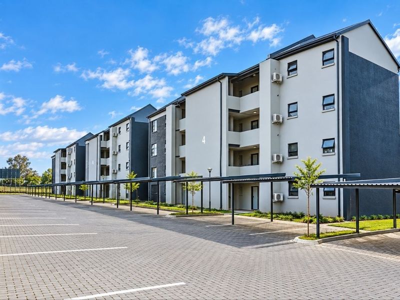 Modern multi-story apartment complex featuring paved parking areas with covered bays and well-maintained exterior facades.