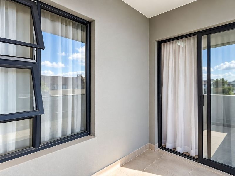 A clean, modern balcony featuring tiled flooring, large sliding glass doors, and dark aluminum-framed windows, offering a bright and well-maintained outdoor space.