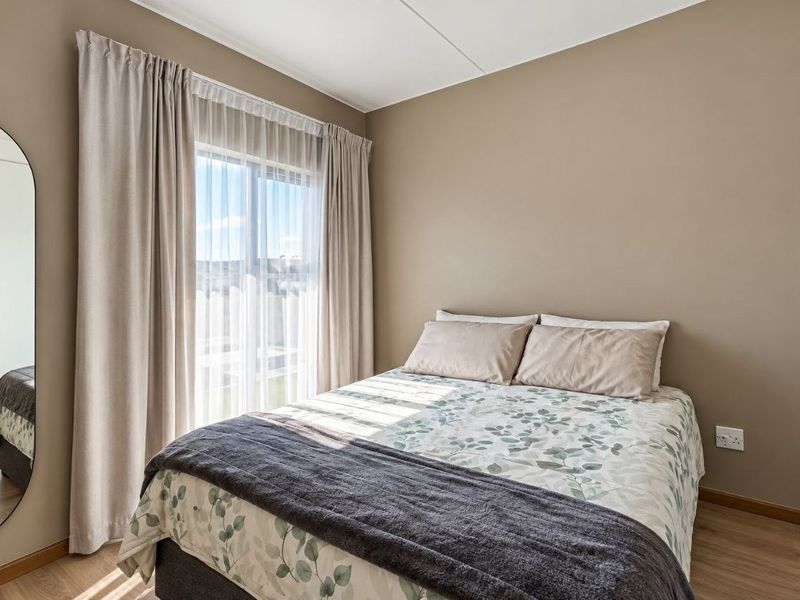 A well-maintained bedroom featuring laminate flooring, neutral wall tones, and a sliding glass door that provides natural light.