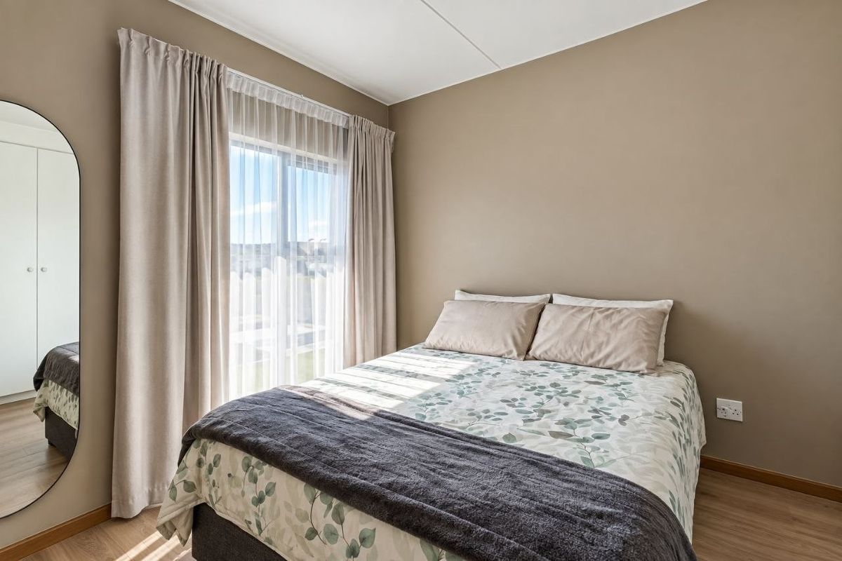 A well-maintained bedroom featuring laminate flooring, neutral wall tones, and a sliding glass door that provides natural light.