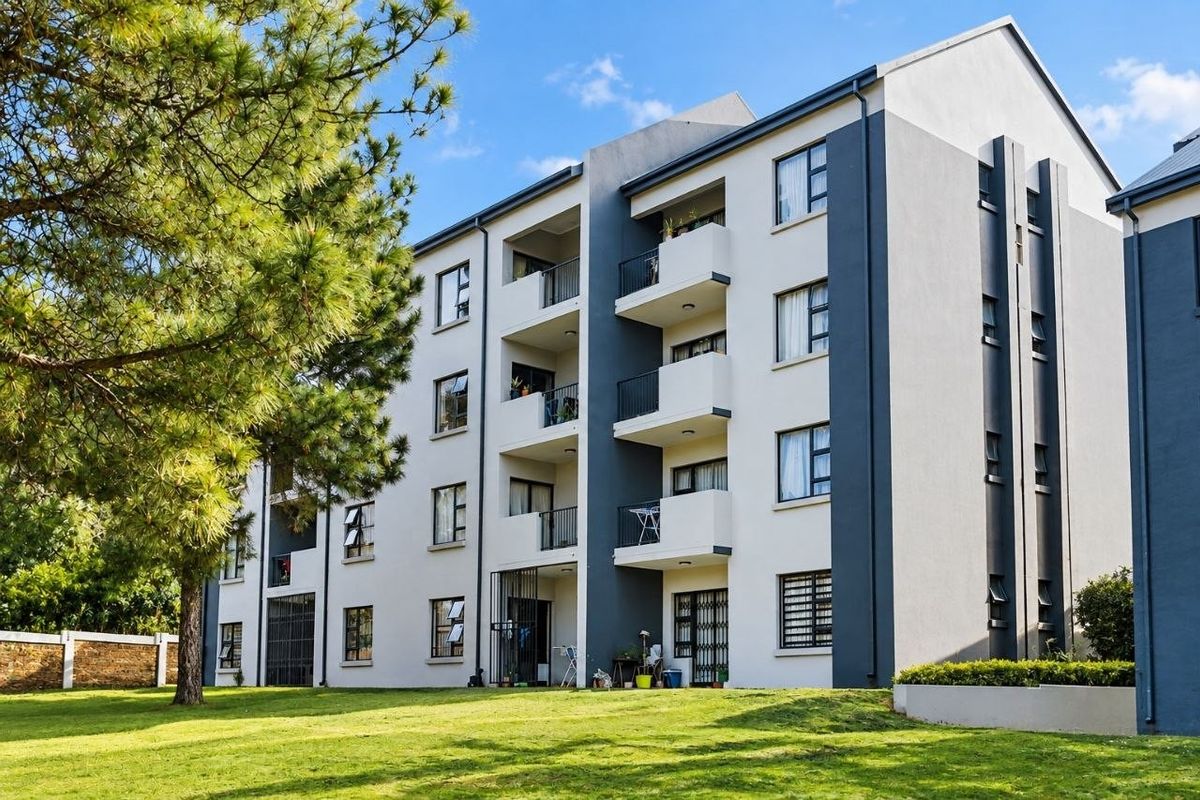 A multi-story apartment building exterior featuring private balconies, modern grey and white facade finishes, and well-maintained surrounding lawn areas.