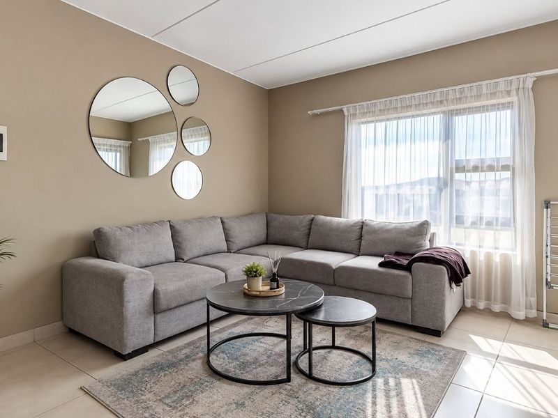 A well-lit living room featuring neutral wall tones, tiled flooring, and a large window with sheer curtains, providing a comfortable and inviting atmosphere.