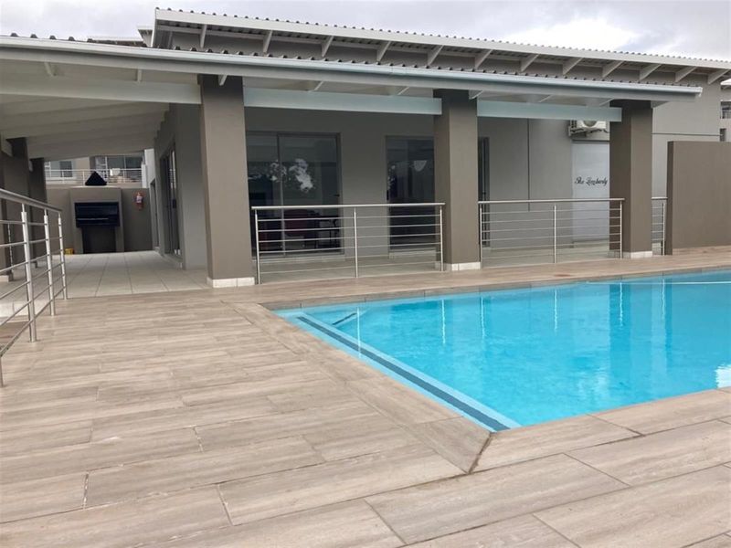 A well-maintained outdoor pool area featuring a tiled deck, stainless steel balustrades, and a covered patio with a built-in braai.