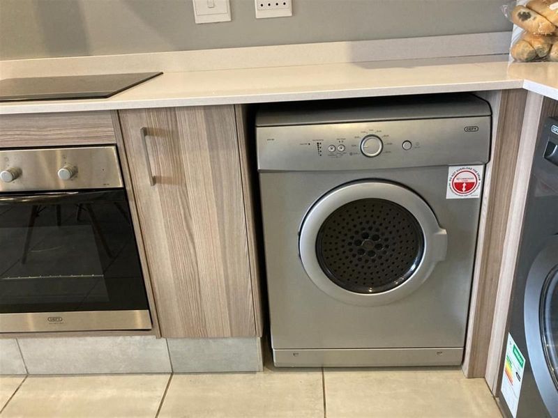 Modern kitchen featuring light wood-grain cabinetry, stone countertops, a built-in oven, electric hob, and an integrated tumble dryer.