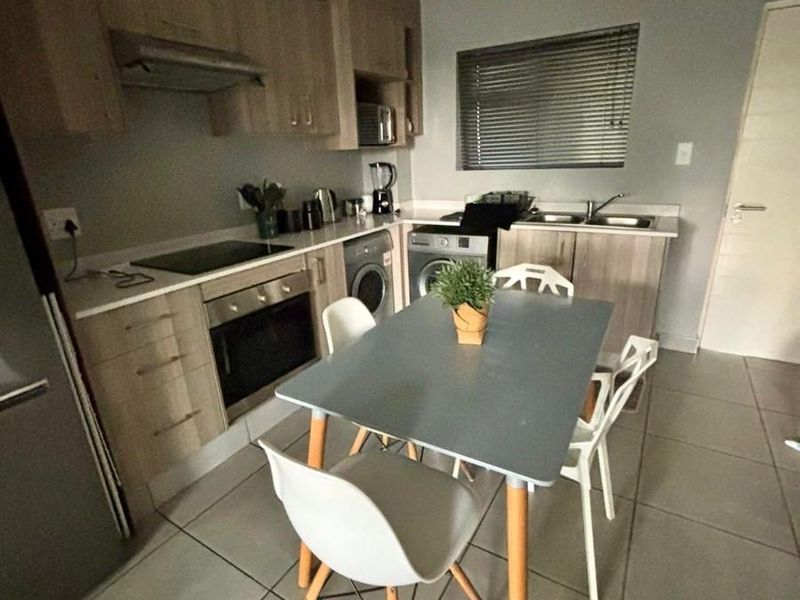 A functional kitchen featuring light wood cabinetry, integrated appliances including an oven and hob, double sink, and neutral tiled flooring.