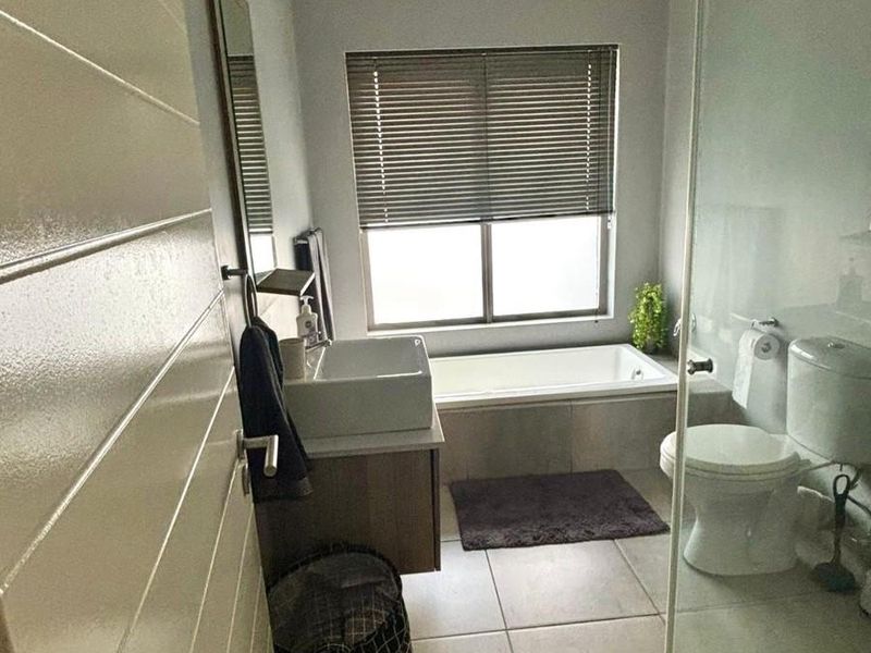 Modern bathroom featuring a built-in vanity with vessel sink, a glass-enclosed shower, and a built-in bathtub with neutral floor tiling.