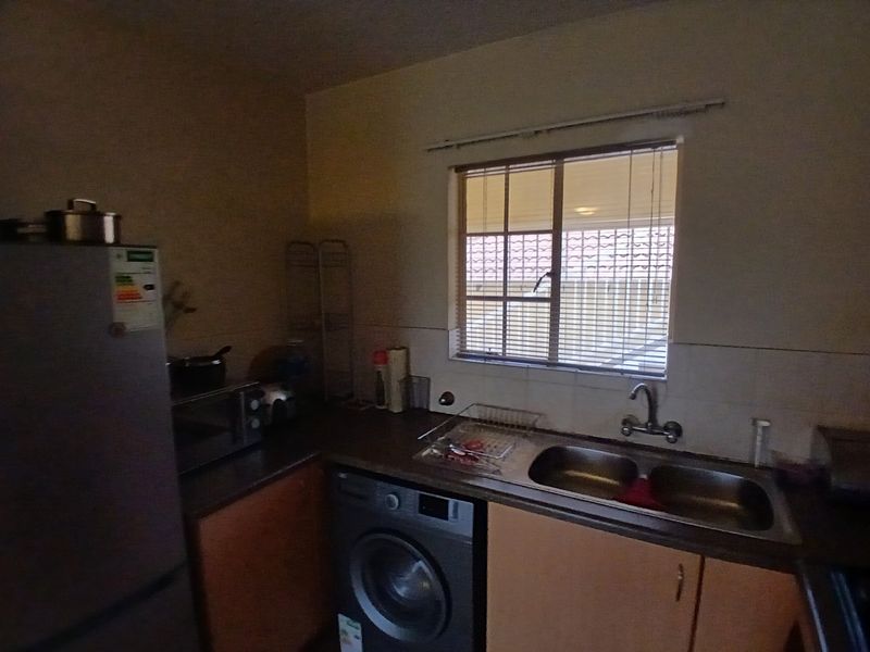 A functional kitchen area featuring a double bowl stainless steel sink, tiled splashback, and built-in cabinetry with space for under-counter appliances.