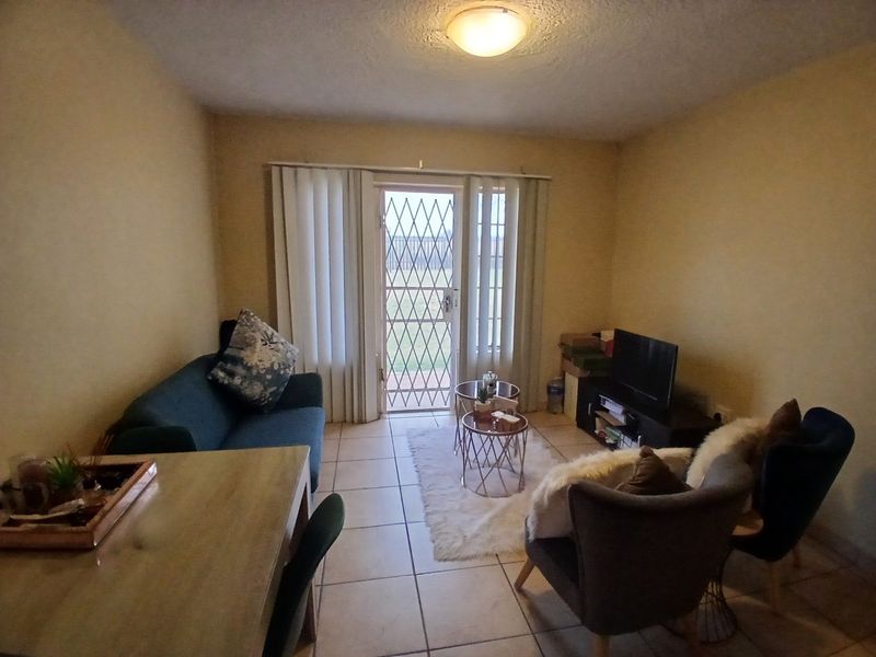 A functional living room featuring tiled flooring, a security gate, and a sliding glass door providing access to the exterior.