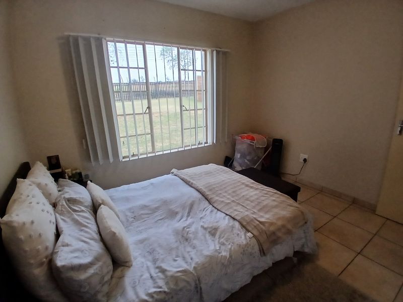 A functional bedroom featuring tiled flooring, a window with security bars, and vertical blinds, offering a simple and practical living space.