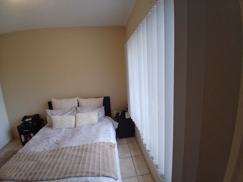 A bedroom featuring neutral wall tones, tiled flooring, and vertical blinds providing natural light control.