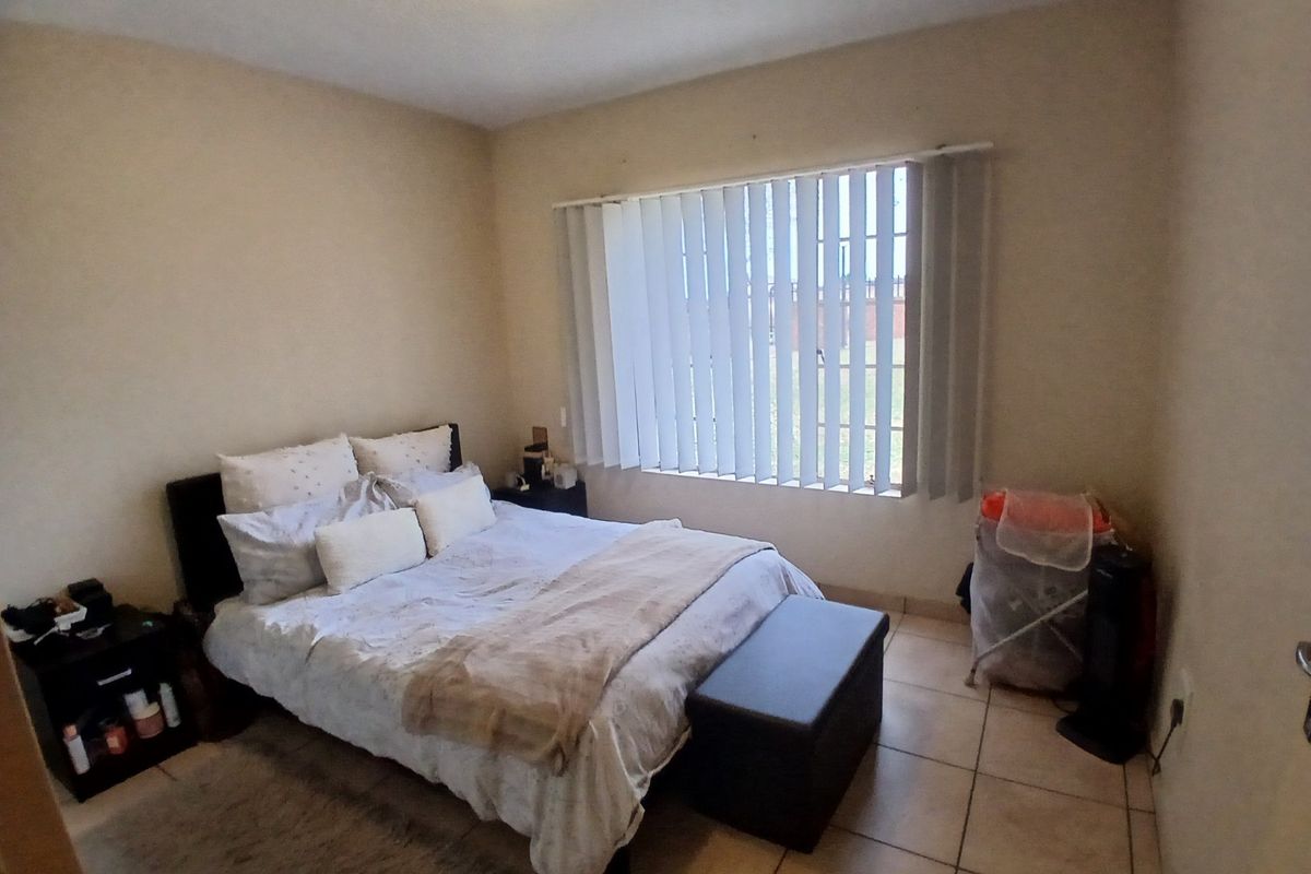 A standard bedroom featuring tiled flooring and vertical window blinds, providing a functional and neutral space.