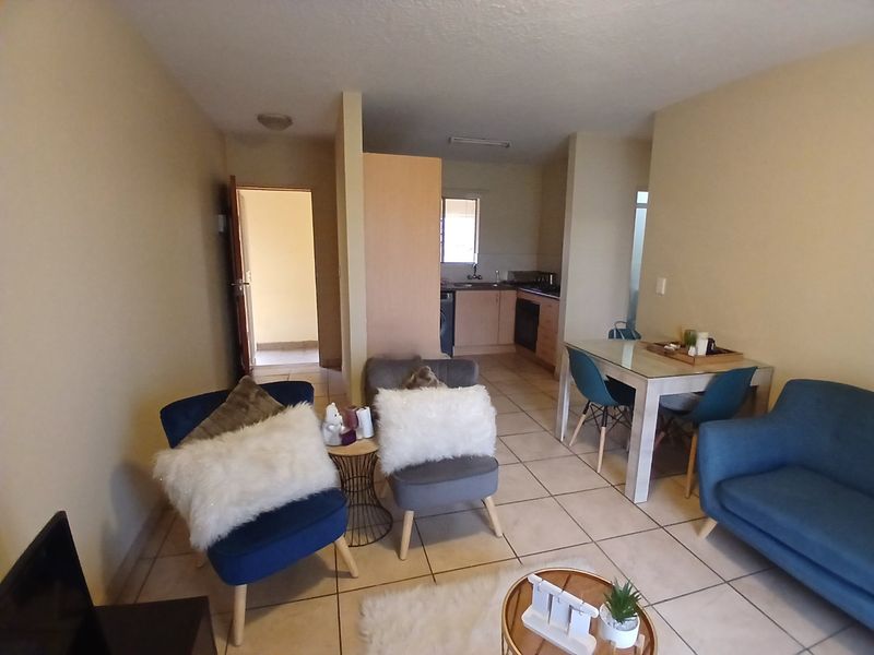 Open-plan living and dining area featuring tiled flooring and a compact kitchen with built-in cabinetry and oven.