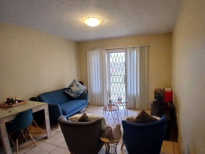 A living room featuring tiled flooring and a sliding door with a security gate, providing access to the exterior.
