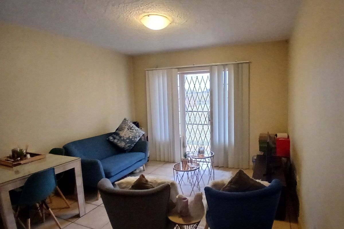 A living room featuring tiled flooring and a sliding door with a security gate, providing access to the exterior.
