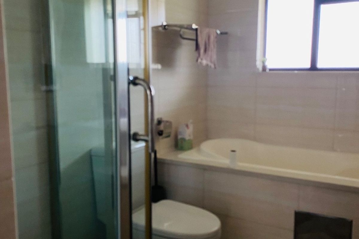 A functional bathroom featuring a shower enclosure, bathtub, and toilet with neutral wall and floor tiling.