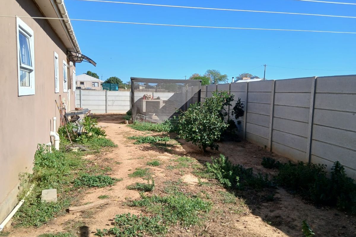 Rear garden area featuring a precast concrete boundary wall, built-in braai structure, and open yard space with potential for landscaping.