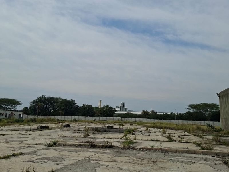 A large, vacant industrial concrete yard featuring a perimeter wall and significant surface wear, suitable for redevelopment or storage.
