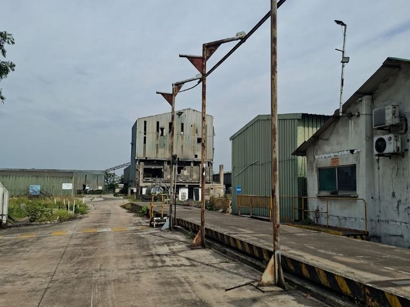 Industrial site featuring a concrete loading dock, metal support structures, and weathered warehouse buildings with visible signs of age and structural wear.