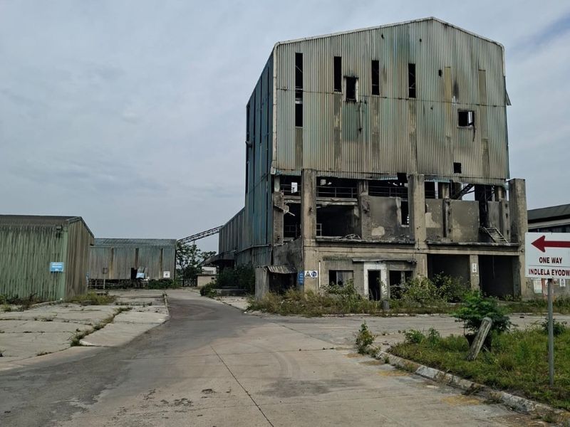 An industrial site featuring a large, weathered corrugated metal warehouse structure with significant signs of age and structural deterioration.
