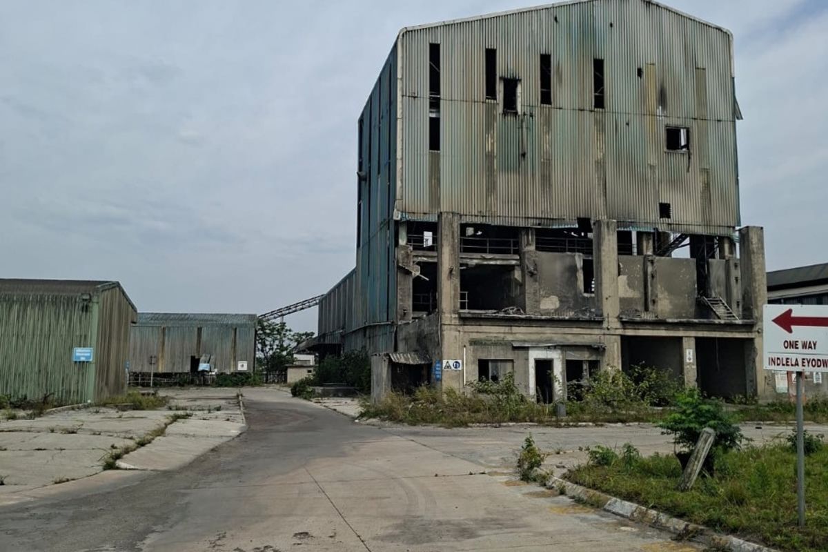 An industrial site featuring a large, weathered corrugated metal warehouse structure with significant signs of age and structural deterioration.