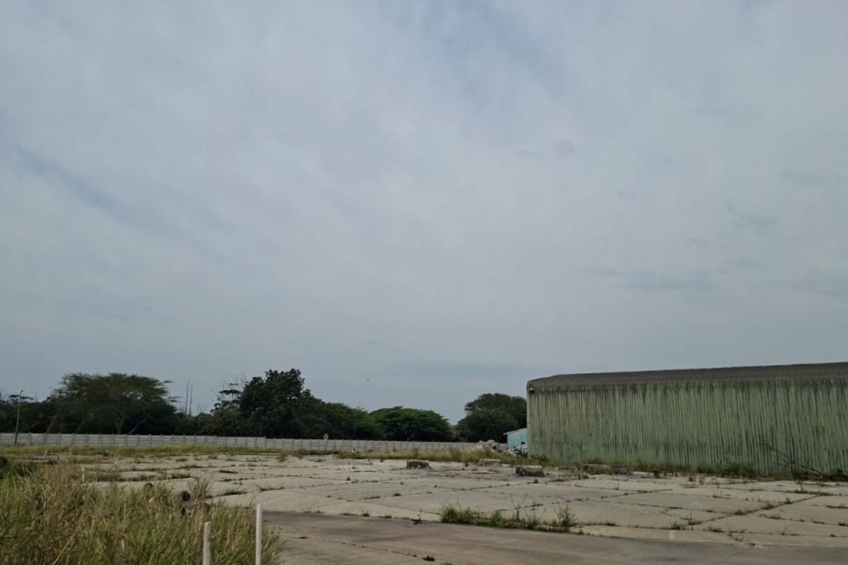 Expansive industrial yard featuring concrete paving and large metal-clad structure, suitable for storage or logistics operations.