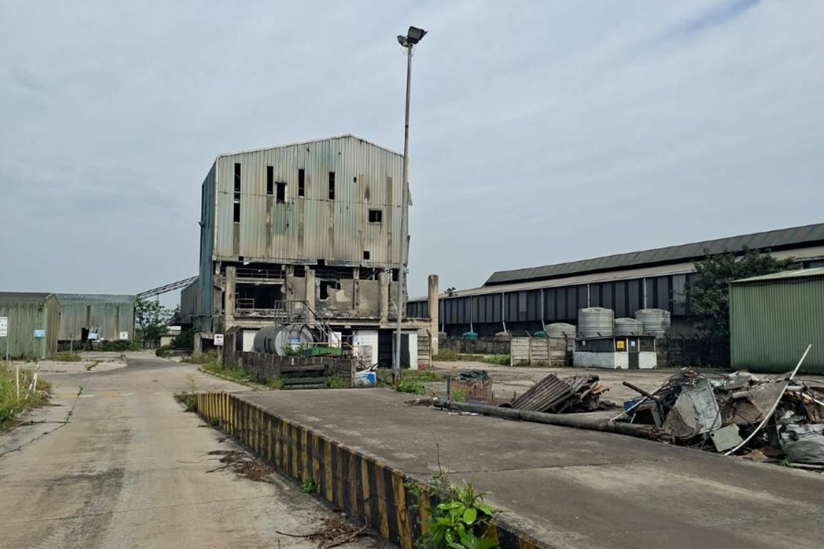 Industrial site featuring a large concrete loading bay, weathered metal-clad structures, and extensive paved yard space in need of significant maintenance.