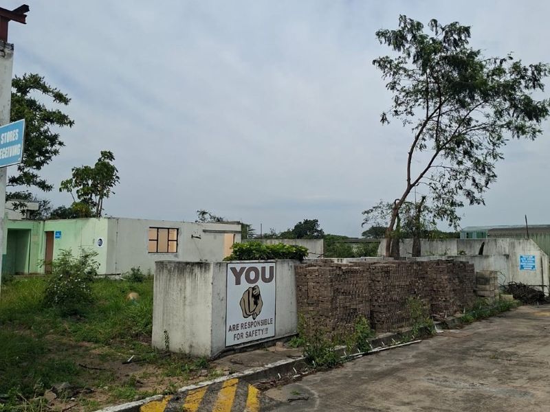 Industrial yard area featuring concrete paving, boundary walls, and signage, showing signs of wear and requiring maintenance.