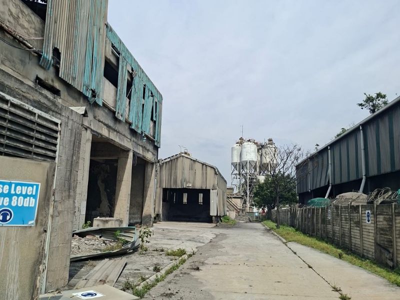 View of an industrial site featuring weathered corrugated metal structures, concrete paving, and large storage silos within a fenced yard area.