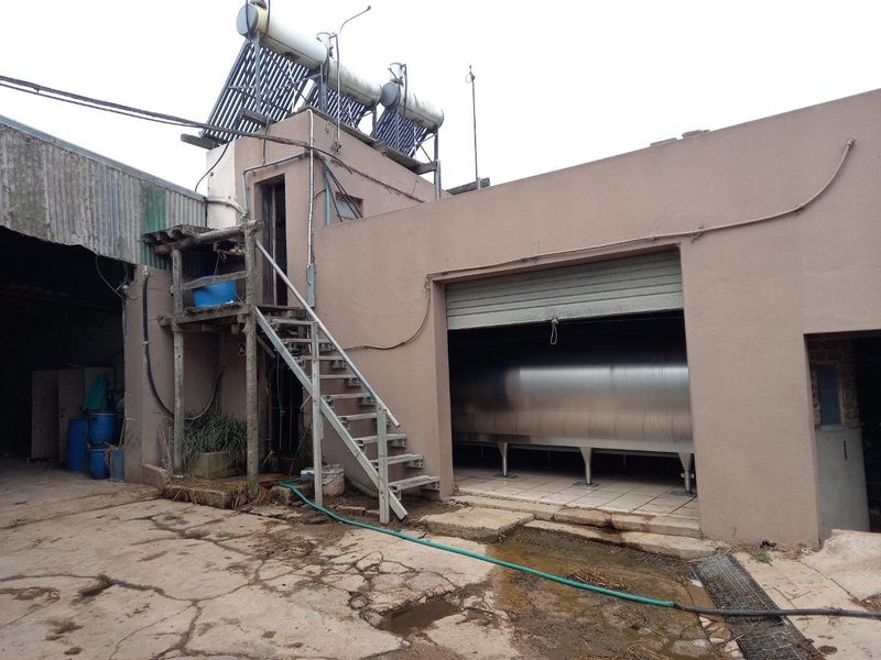 Utility area featuring a large stainless steel milk cooling tank, solar water heating system, and external metal staircase on a farm property.