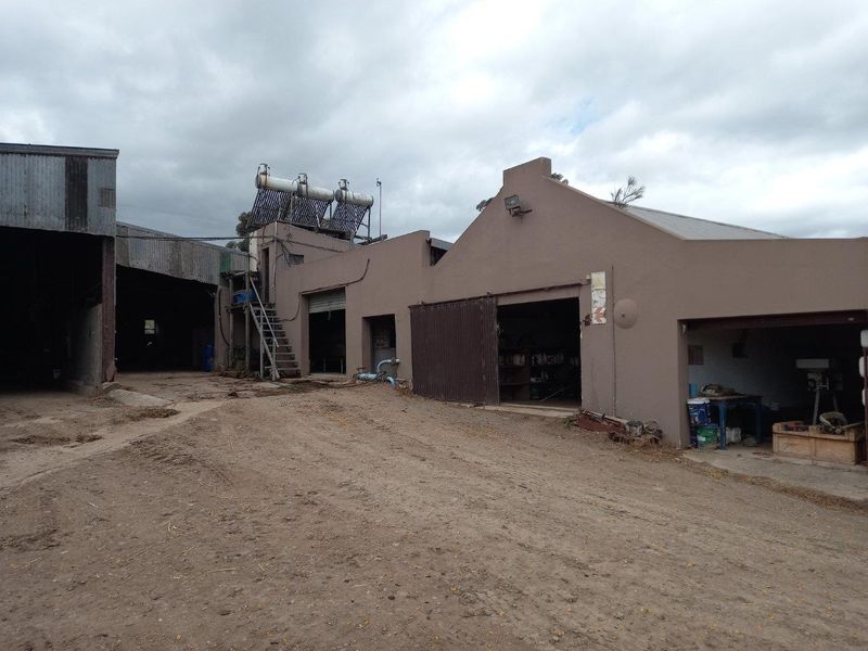 Rear view of farm outbuildings featuring plastered masonry walls, corrugated metal roofing, and an installed solar water heating system.