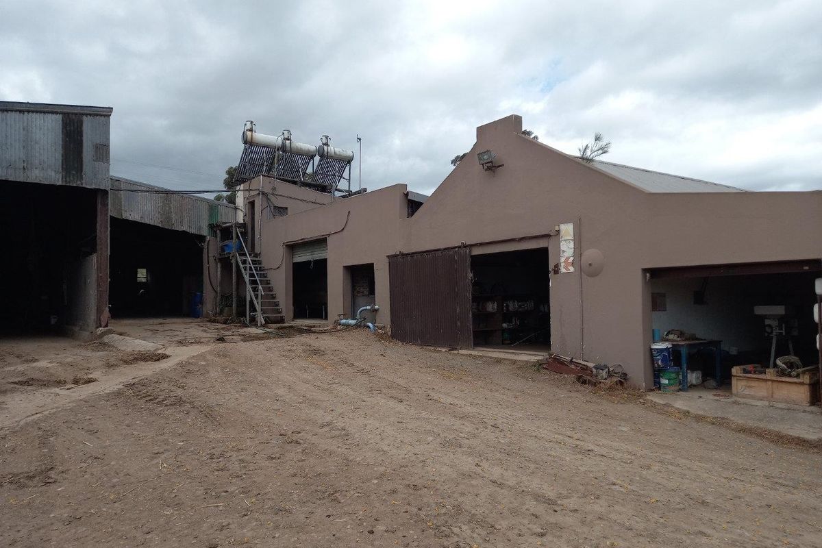 Rear view of farm outbuildings featuring plastered masonry walls, corrugated metal roofing, and an installed solar water heating system.