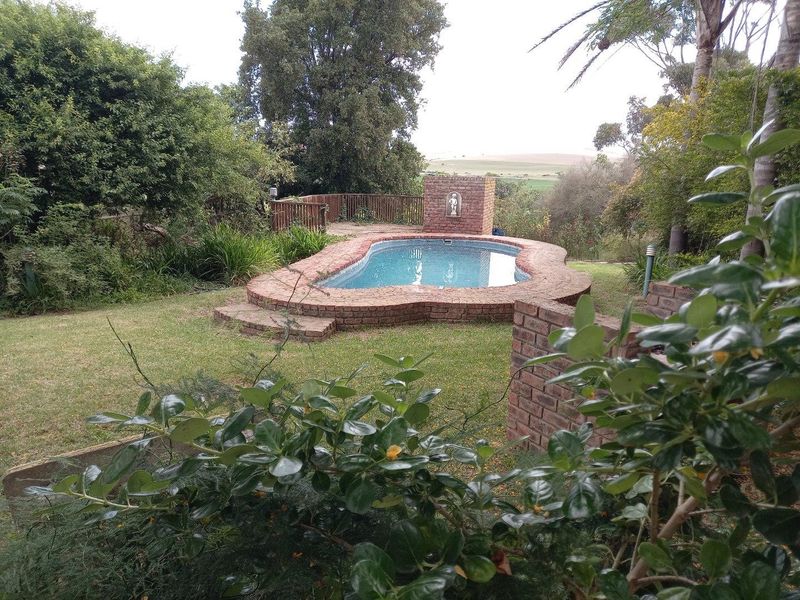 A landscaped outdoor pool area featuring a brick-edged swimming pool with a built-in water feature, set within a garden with scenic rural views.