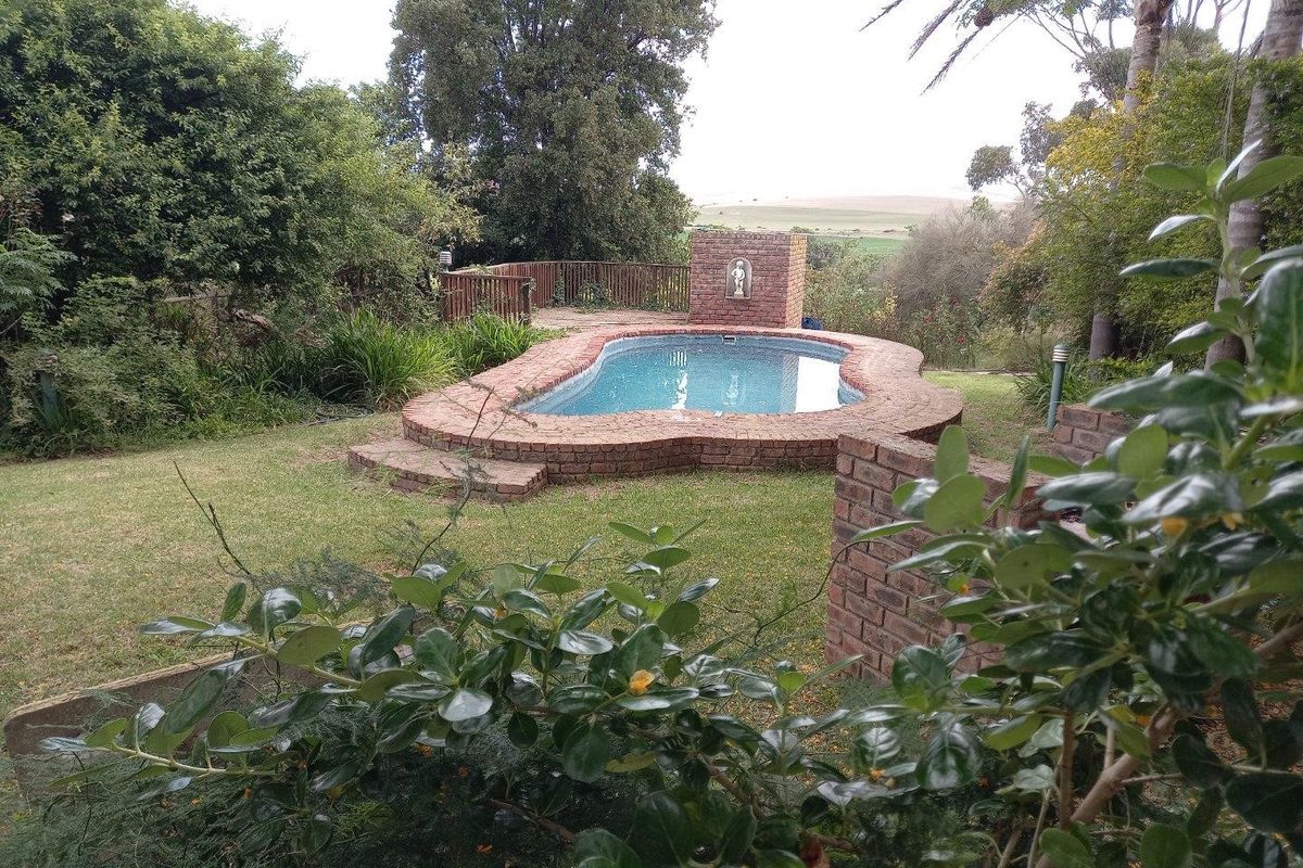 A landscaped outdoor pool area featuring a brick-edged swimming pool with a built-in water feature, set within a garden with scenic rural views.
