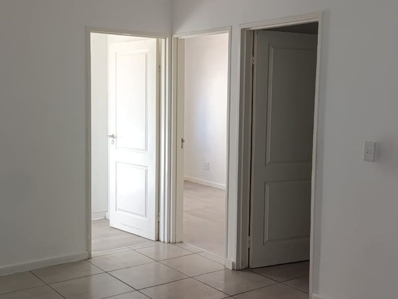 A neutral, empty hallway featuring tiled flooring and access to multiple rooms through standard internal doors.