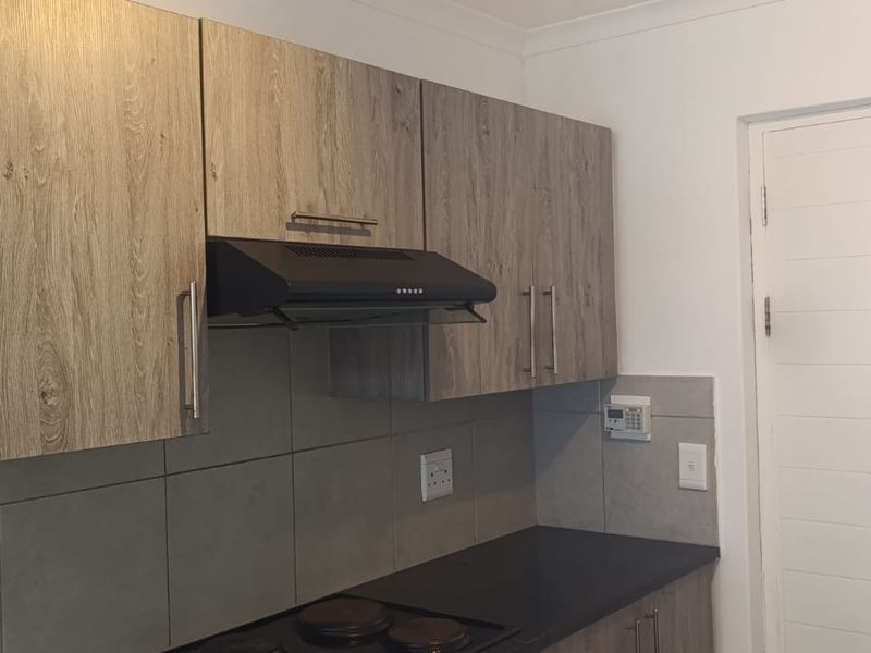 A clean, modern kitchen featuring wood-look cabinetry, a built-in extractor fan, electric hob, and neutral tile backsplash.