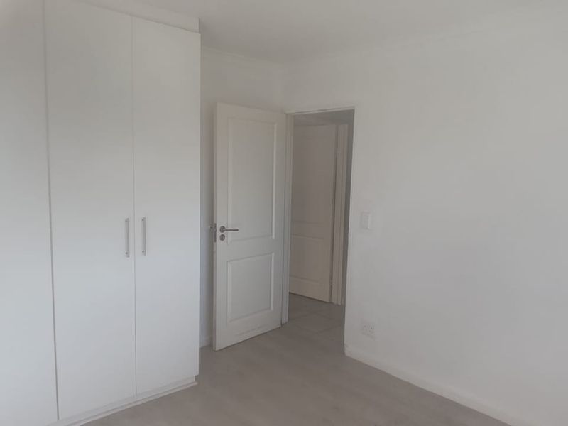 A bright, empty bedroom featuring neutral laminate flooring and white built-in cupboards, offering a clean and versatile space ready for personalization.