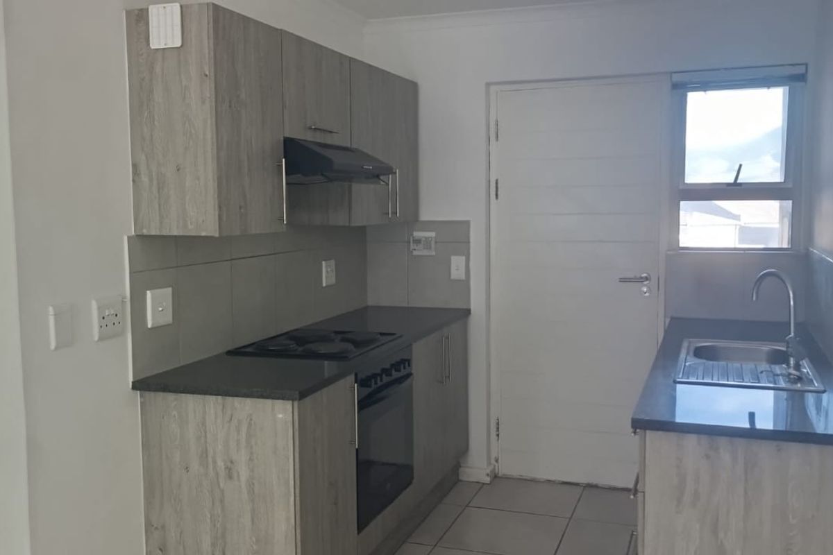 A functional kitchen featuring modern grey laminate cabinetry, dark stone countertops, built-in oven, electric hob, and a stainless steel sink with tiled flooring.