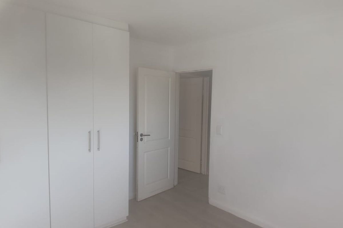 A bright, empty bedroom featuring neutral walls, laminate flooring, and ample built-in cupboard storage space.