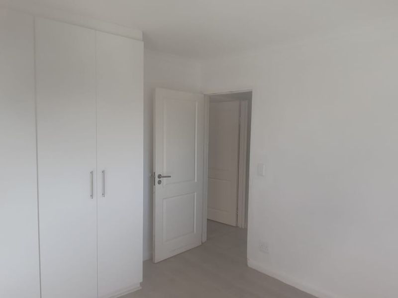 A bright, empty bedroom featuring neutral walls, laminate flooring, and ample built-in cupboard storage space.