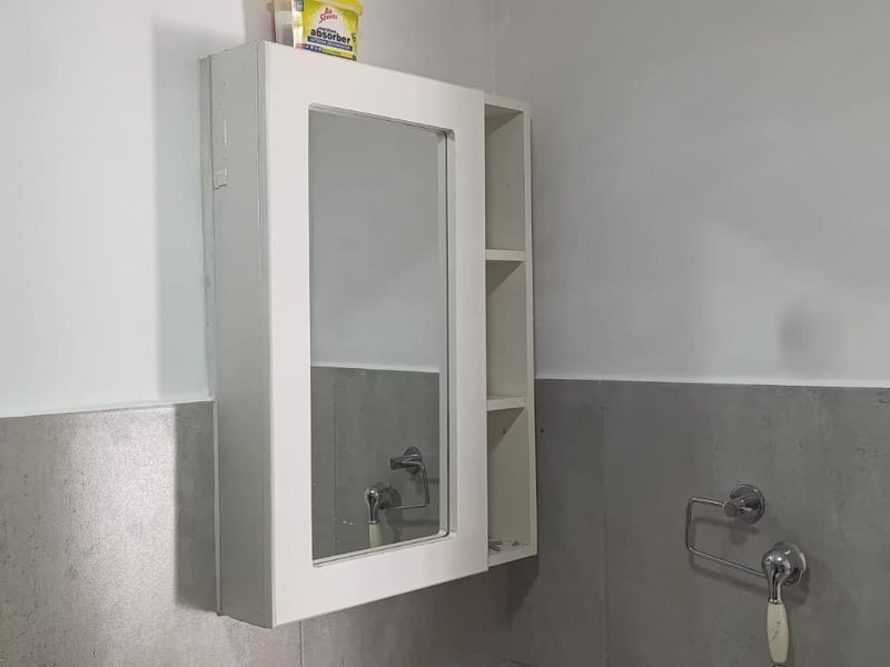 A functional bathroom space featuring a wall-mounted medicine cabinet and neutral grey wall tiling.