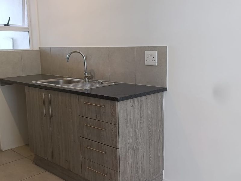 A clean, modern kitchen area featuring wood-look cabinetry, a stainless steel sink, and neutral tiled splashbacks in a well-maintained space.