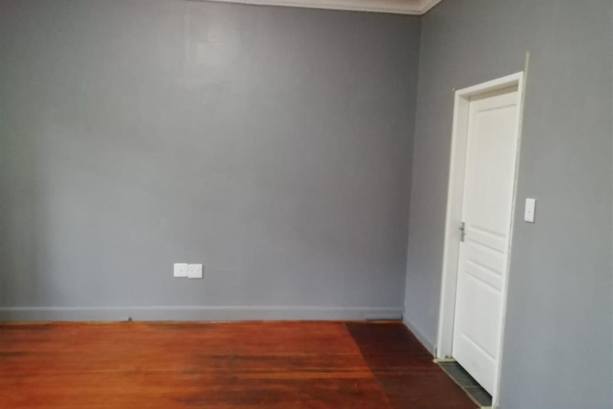 An empty bedroom featuring polished hardwood flooring, grey painted walls, and a classic white panelled door with decorative cornice detailing.