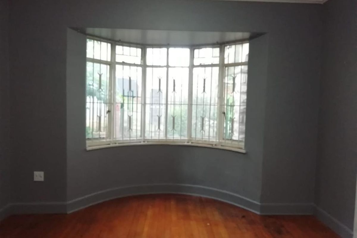 An empty living room featuring polished hardwood flooring and a prominent bay window with integrated security bars.