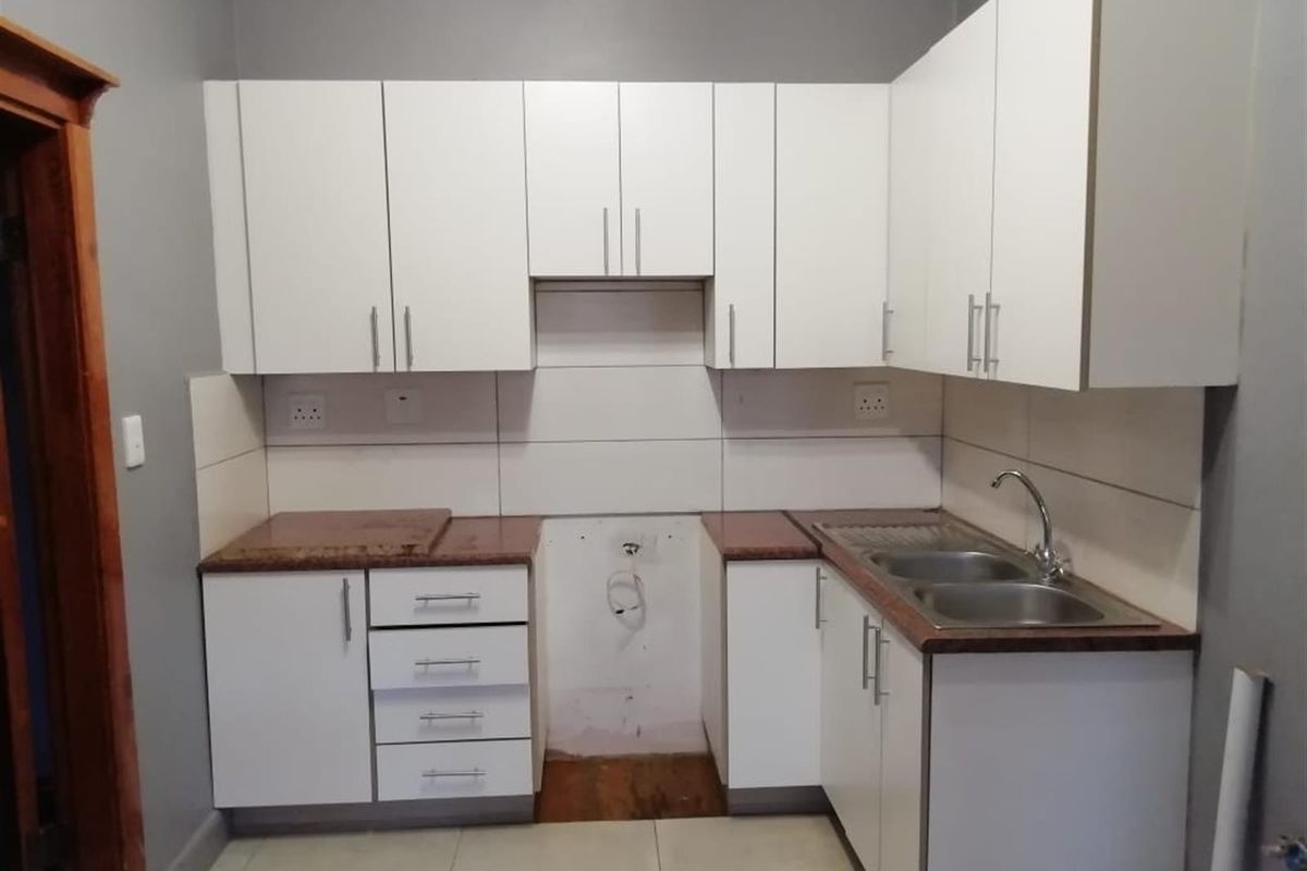 A functional kitchen featuring white cabinetry, laminate countertops, a double bowl stainless steel sink, and tiled backsplash with dedicated space for appliances.