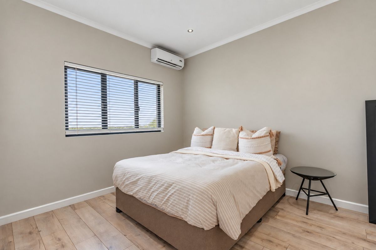 A well-maintained bedroom featuring timber-look flooring, a split-system air conditioner, and neutral wall tones, providing a clean and comfortable living space.