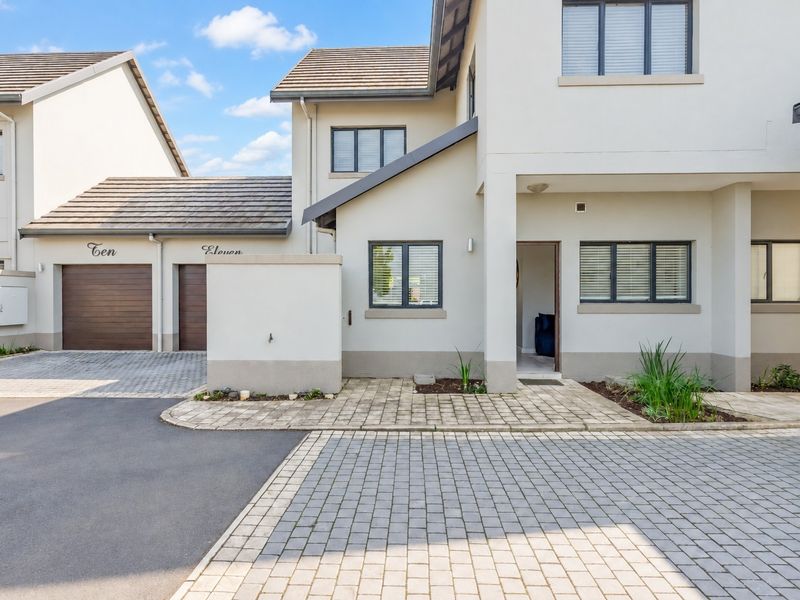 Front elevation of a modern townhouse featuring a paved driveway, double garage, and a covered entrance with neutral exterior finishes.