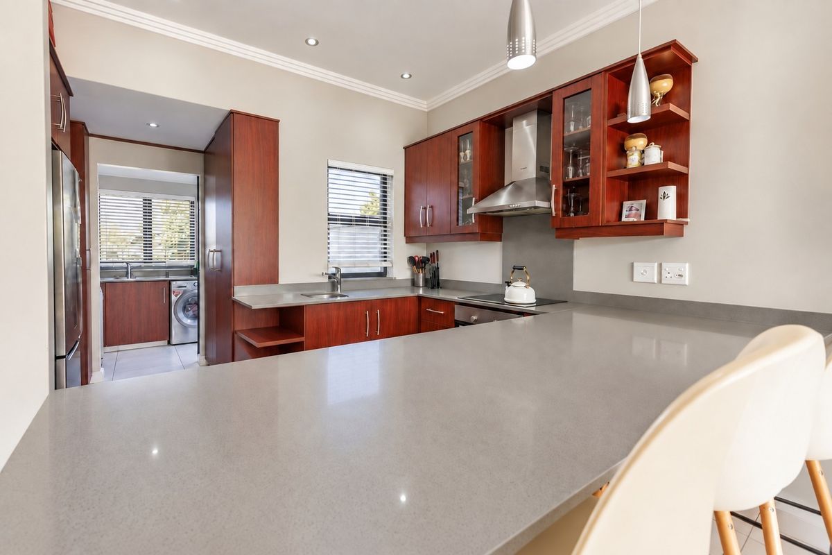 Modern kitchen featuring rich wood cabinetry, stone countertops, integrated appliances, and a breakfast bar, with an adjacent scullery area visible.